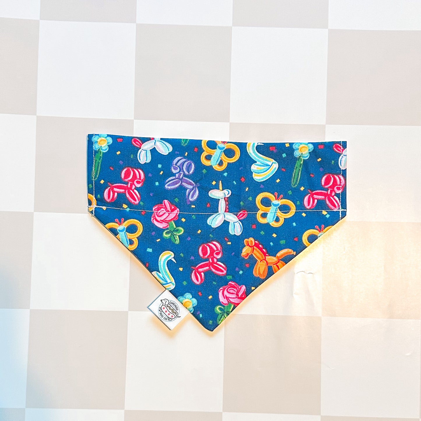 Colorful dog bandana with balloon animal design on a checkered background